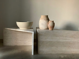 Two triangle shape travertine coffee tables with some pottery on.