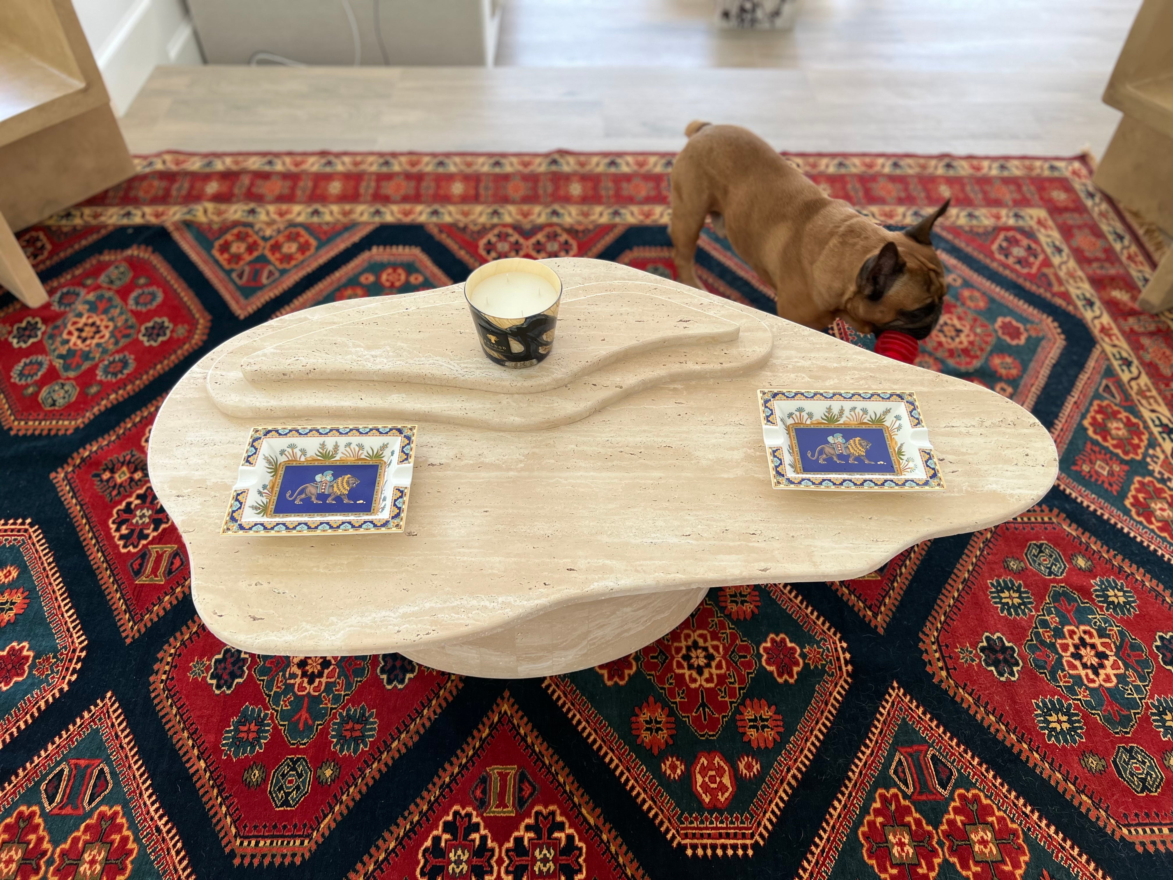 Top view of 3 layer natural light beige travertine wavy organic shape coffee table on red Patterned rug.