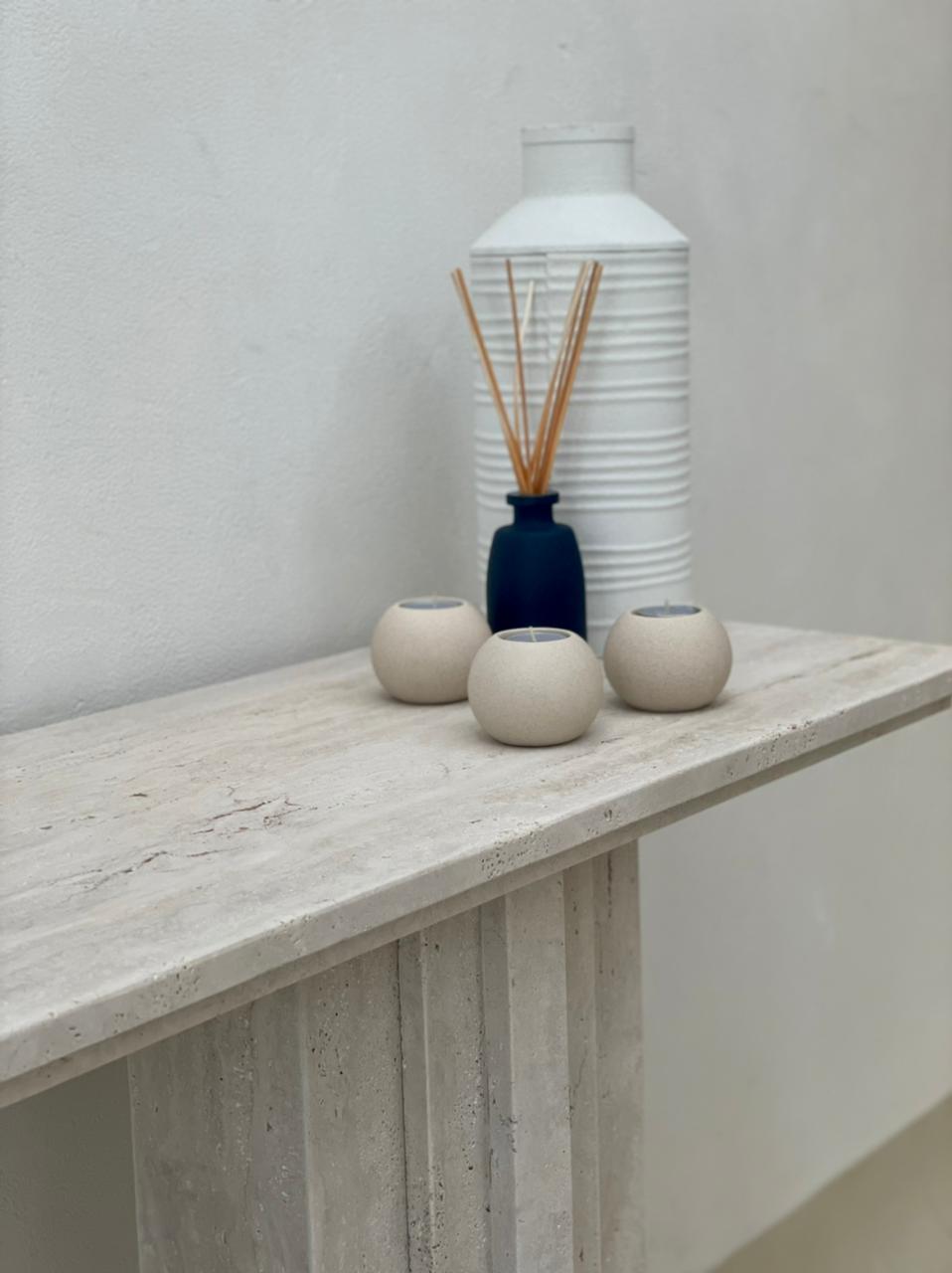 Close up look of travertine console table with stepped details. displaying candles and white vase.