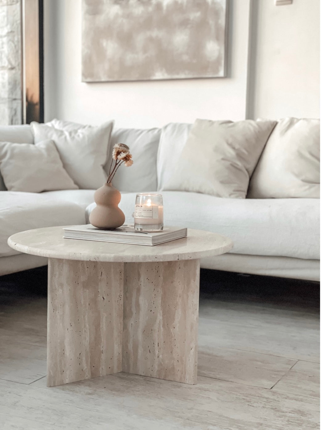 Round travertine coffee table with candle and flower vase, in front of sofa