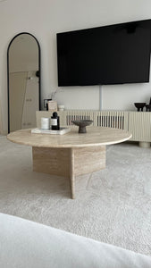 Large round travertine coffee table with decor items on.