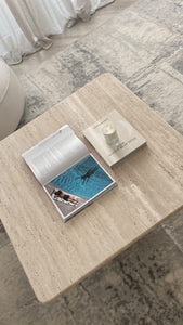 Travertine coffee table and magazine, book and candle displayed.