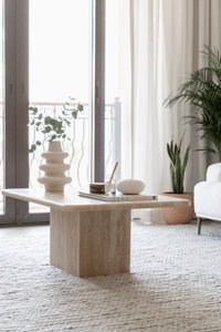 Rectangle coffee table in beige travertine with decor pieces in front of window