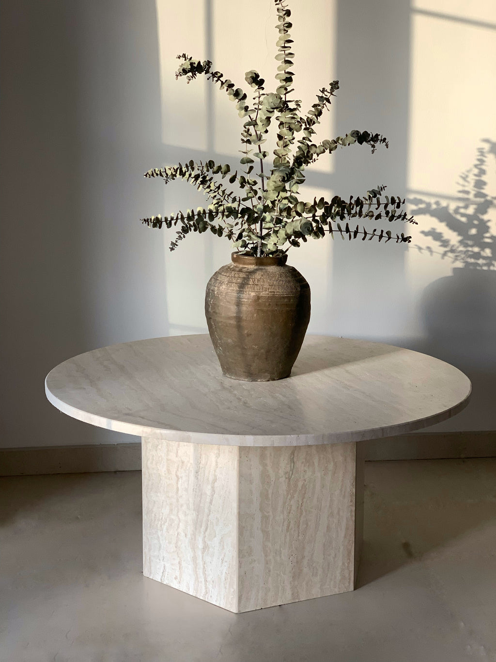 Round light beige coffee table with hexagonal base, displaying vase with stems.