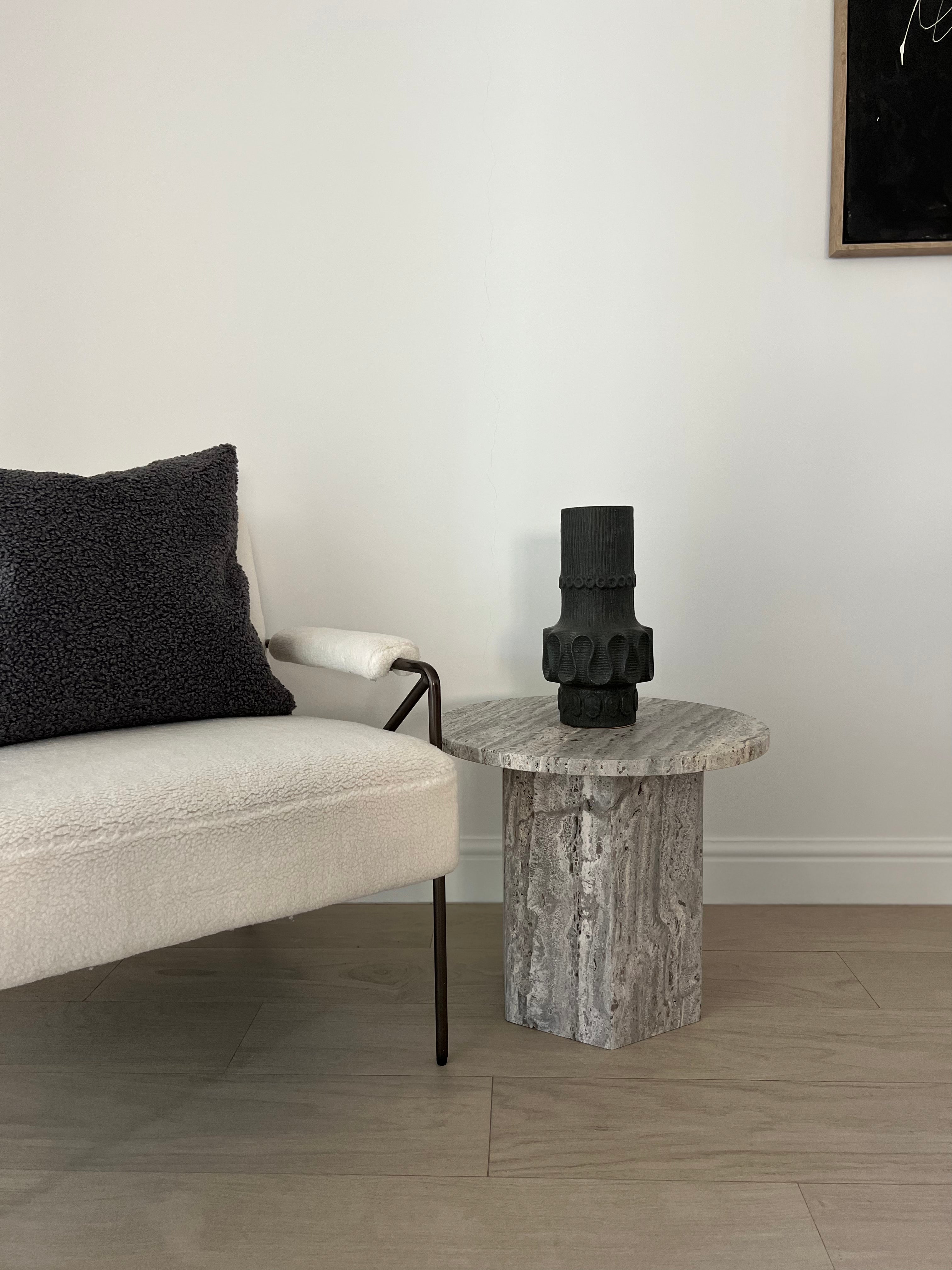 Silver travertine round side table with hexagonal base next to a comfy chair.