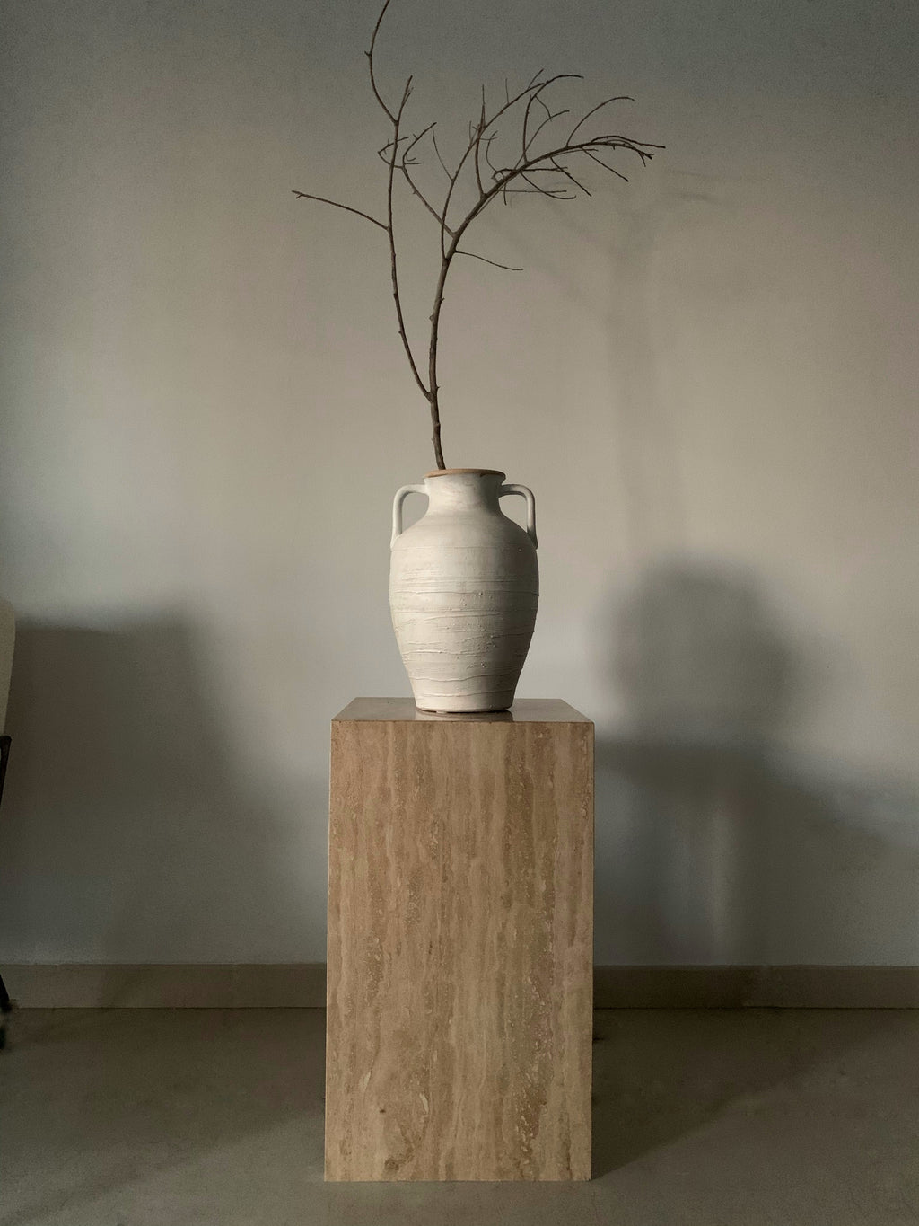 Caramel beige travertine cube plinth table with white pottery vessle.