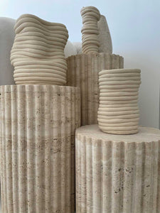 Close up of curved fluted travertine stone plinths in natural and textured stone.