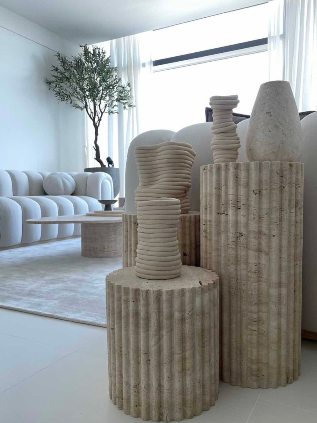 3 varying height travertine fluted pedestals, in stylish room 