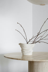 Close up of beige round travertine dining table with a cole and cinder vase.